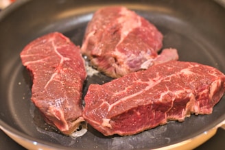 three steaks are cooking in a frying pan
