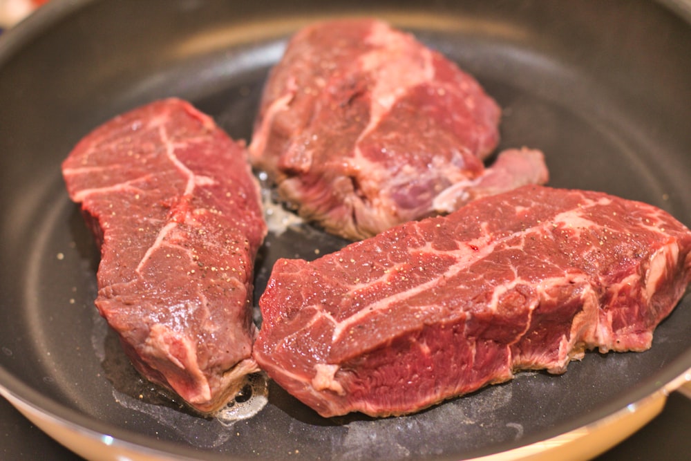three steaks are cooking in a frying pan