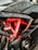 A close-up view of a motorcycle's engine area featuring a red frame with the word 'RACESPEC' written on it. Various components such as hoses, bolts, and the shiny black exterior of a fuel tank are visible.