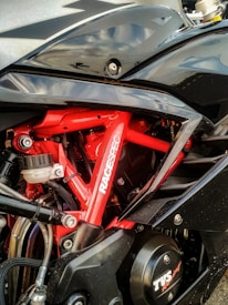 A close-up view of a motorcycle's engine area featuring a red frame with the word 'RACESPEC' written on it. Various components such as hoses, bolts, and the shiny black exterior of a fuel tank are visible.