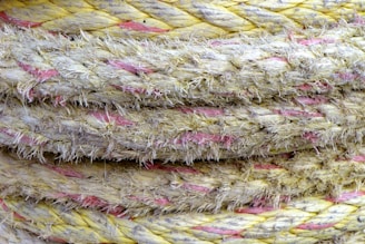 Close-up view of several twisted, frayed, and thick ropes stacked together. The ropes are primarily yellow with interwoven pink strands, giving them a rugged and weathered appearance.