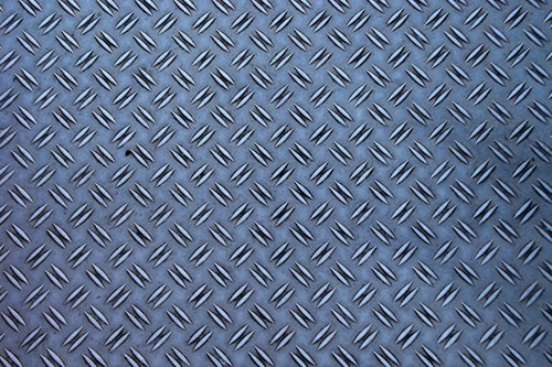 A metal surface with a diamond plate pattern, showing a series of raised, elongated shapes uniformly distributed across the surface.