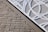 A textured brick wall is intersected by a metal panel featuring a geometric cut-out design with circular perforations. The panel is secured with metal screws at the corners.