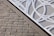 A textured brick wall is intersected by a metal panel featuring a geometric cut-out design with circular perforations. The panel is secured with metal screws at the corners.