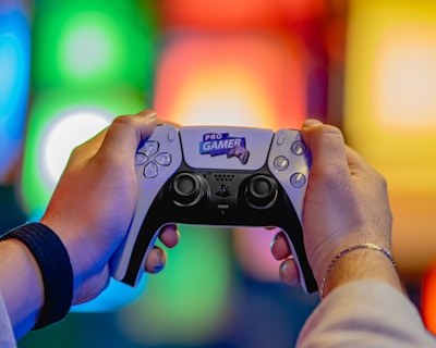 Two hands are holding a gaming controller labeled 'Pro Gamer'. The background is blurred with colorful lights creating a vibrant atmosphere.