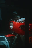Close-up of a motorcycle headlight glowing bright red and white in a dark urban setting.