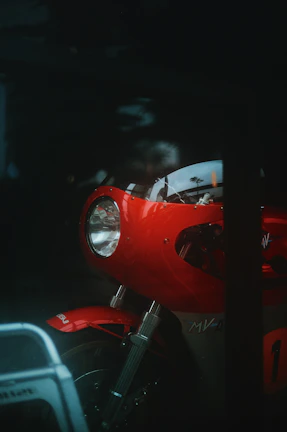 Close-up of a motorcycle headlight glowing bright red and white in a dark urban setting.