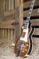 Close-up of a vintage guitar resting against a rustic wooden wall.