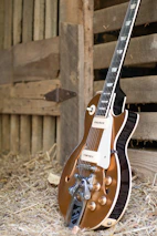 A close-up of a vintage guitar resting against a weathered wooden fence in a southern town.