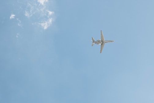 A Boeing small jet soaring above clouds with a clear blue sky backdrop.