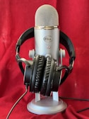 A large, silver microphone is prominently displayed with a pair of black headphones resting on its base. The background is a rich red fabric, creating a striking contrast with the metallic and black elements of the microphone and headphones.