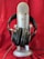 A large, silver microphone is prominently displayed with a pair of black headphones resting on its base. The background is a rich red fabric, creating a striking contrast with the metallic and black elements of the microphone and headphones.