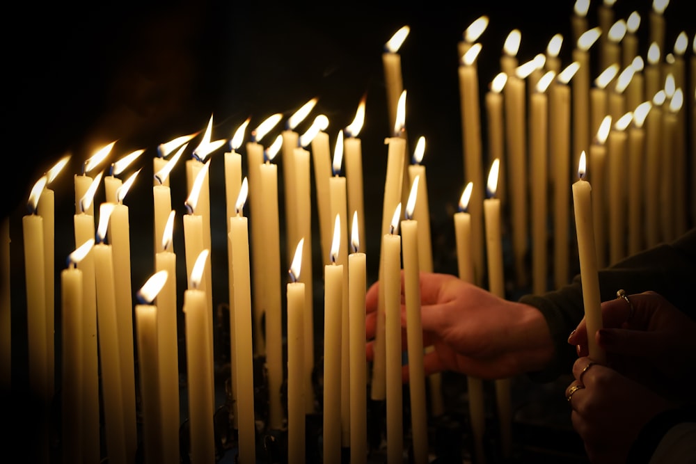 a person holding a lit candle in front of rows of lit candles