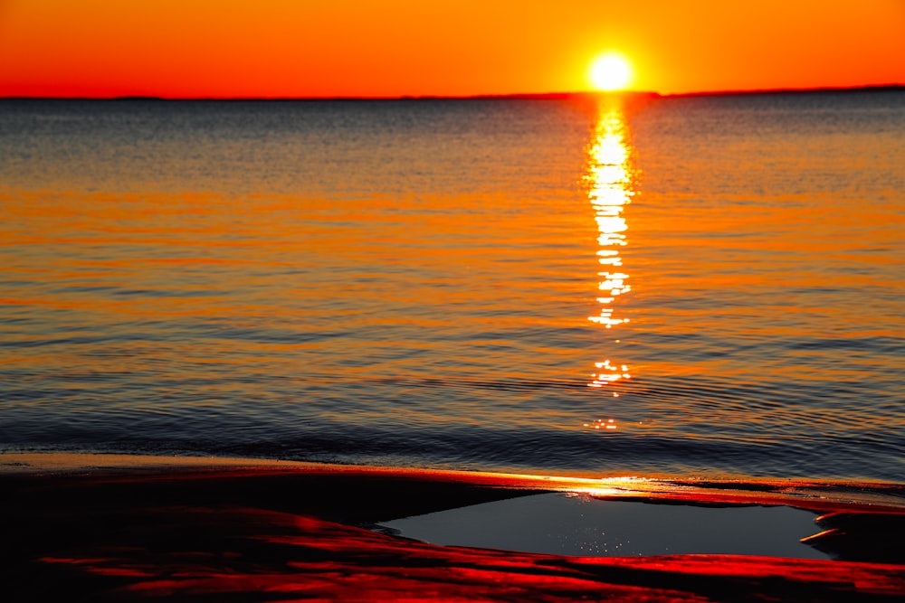 the sun is setting over the water on the beach