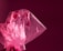 A translucent pink plastic bag with a crinkled texture, contrasting against a deep, maroon background. The lighting highlights the shiny surface and folds of the plastic, creating a dynamic play of light and shadow.