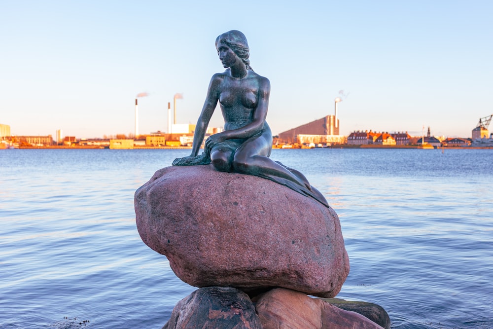 une statue d’une femme assise au sommet d’un rocher