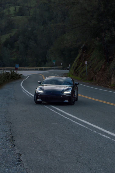 A sleek luxury car winding through the misty hills of Mussoorie at dawn.
