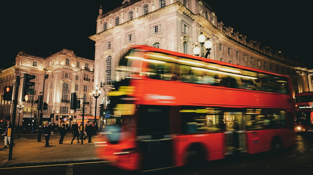 a red double decker bus driving past a tall building