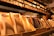 A display of elegantly packaged golden chocolate bars prominently arranged, with a shelf lined with more products in the background. The setting suggests a specialty chocolate shop or a gourmet store with a warm, inviting atmosphere.