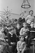 Children gathered around a storyteller sharing Christmas tales by a decorated tree.