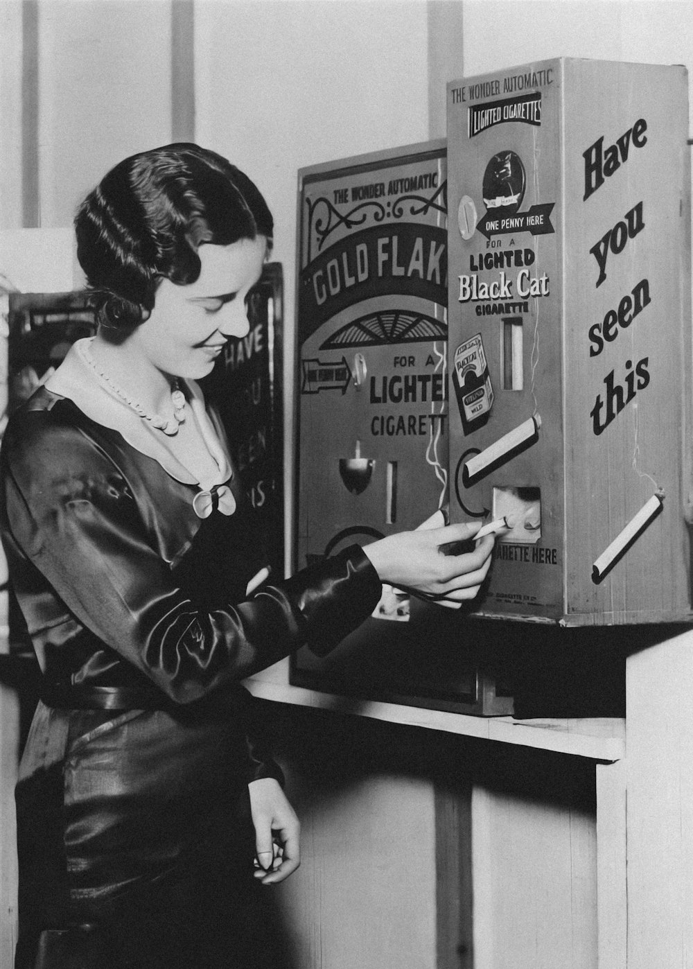 a black and white photo of a woman opening a cigarette machine