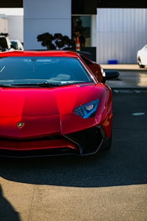 A sleek red sports car parked in front of the Daya Motors showroom under bright sunlight.