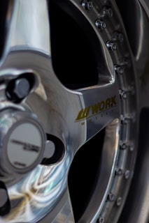 Close-up view of a polished alloy car wheel with the brand 'WORK' visible on the spokes. The wheel features intricate details, including bolts around the rim, reflecting light elegantly.