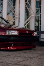 A close-up of a shiny red car parked on a city street under sunlight.