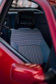 A close-up view of a car's interior, featuring a seat with a plaid fabric pattern. The seat includes a black headrest and is surrounded by a red car door.