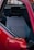 A close-up view of a car's interior, featuring a seat with a plaid fabric pattern. The seat includes a black headrest and is surrounded by a red car door.