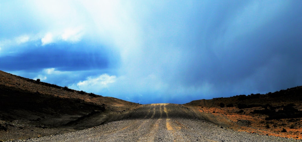 a dirt road in the middle of a desert under a cloudy sky