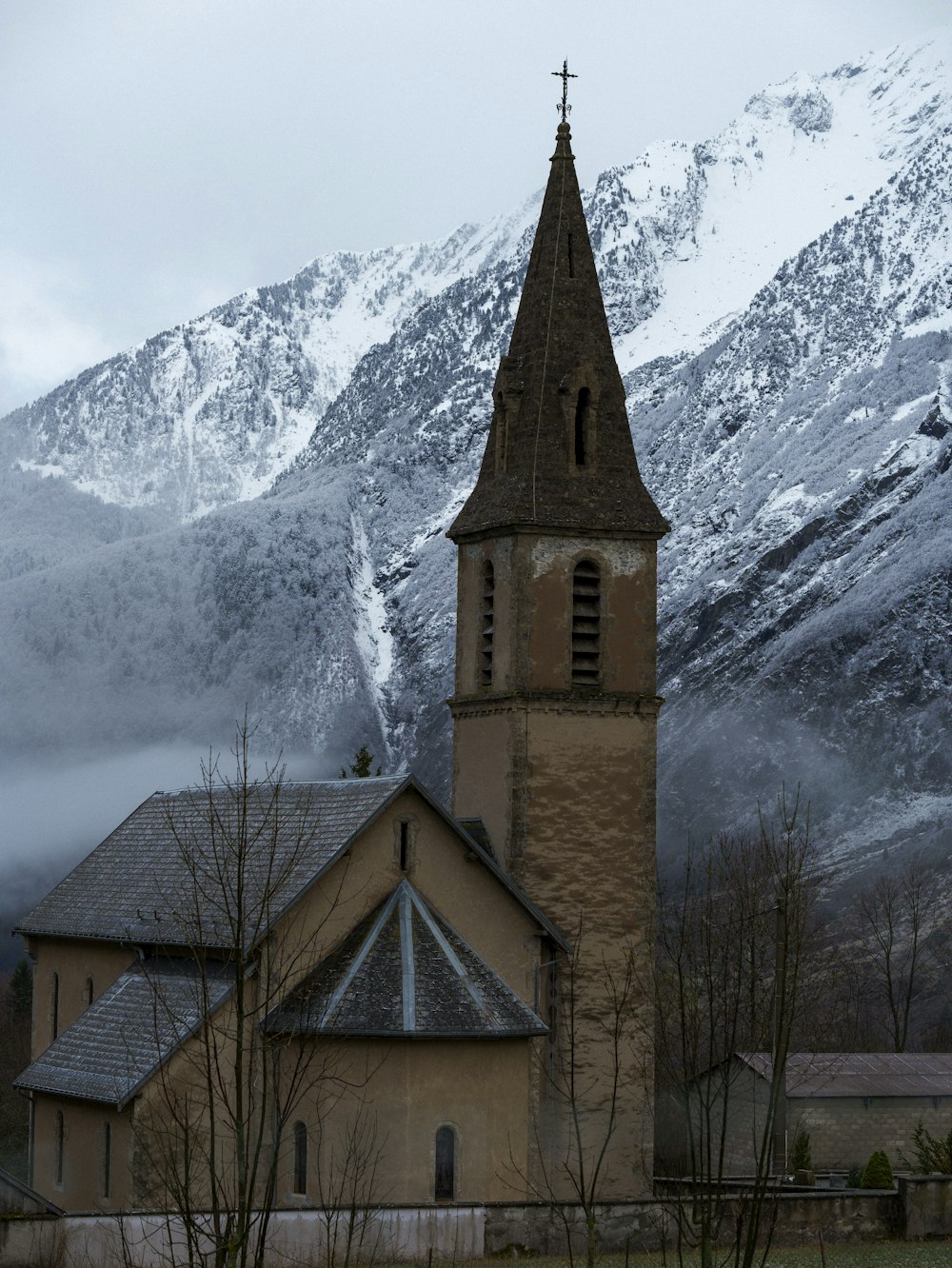 uma igreja com um campanário em frente a uma montanha nevada