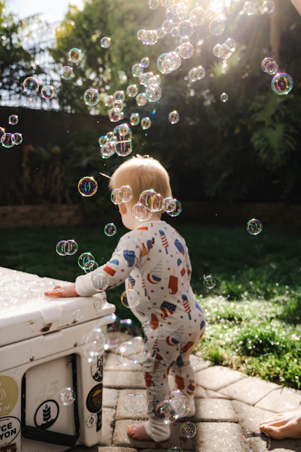 A toddler reaching for soap bubbles in a sunny yard