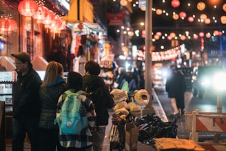 Night scene of a village square lit by lanterns and filled with people.