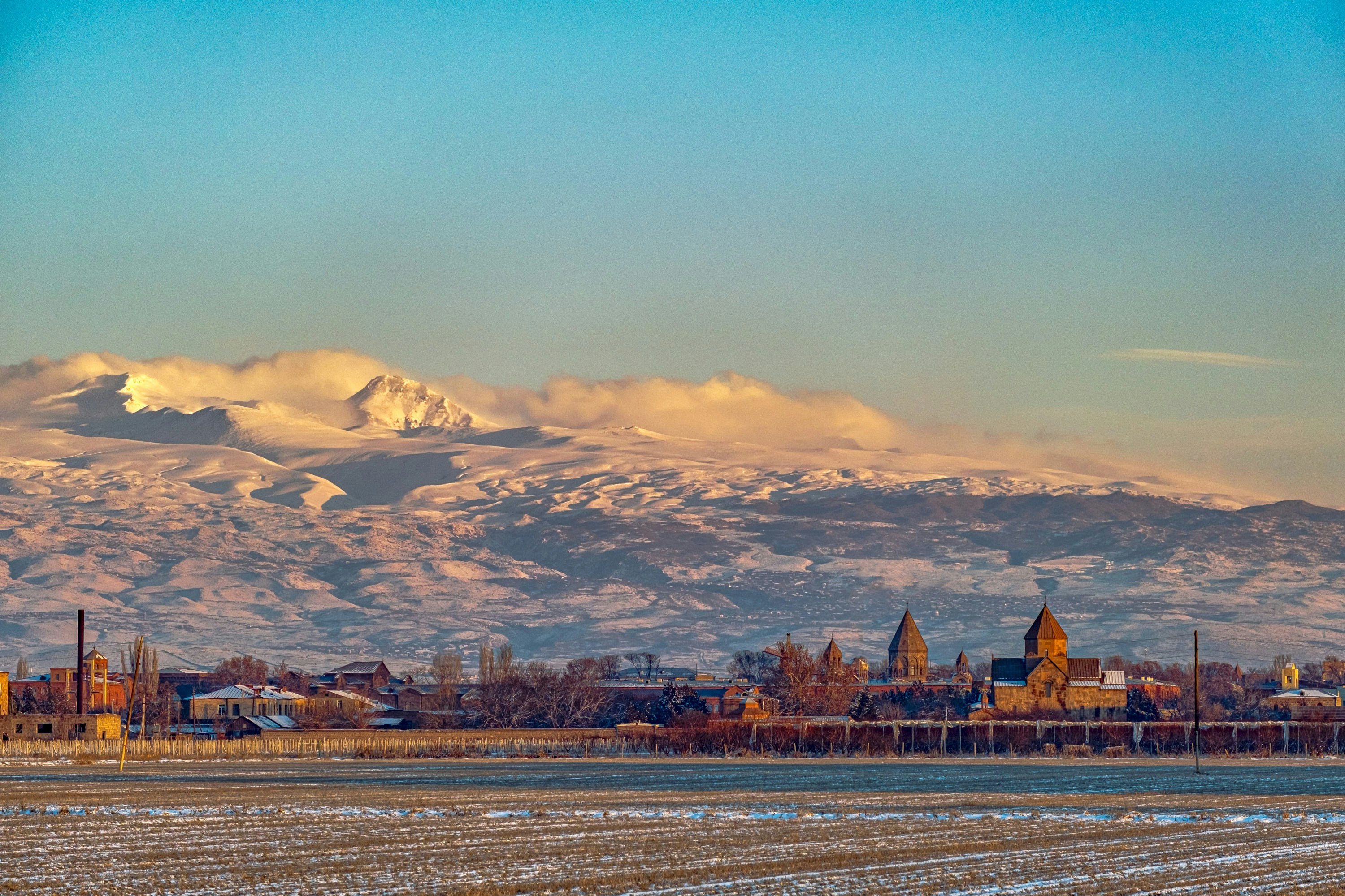 a snowy mountain range in the distance with a town in the foreground