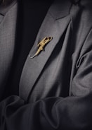 A person is wearing a dark suit jacket adorned with a decorative gold brooch shaped like an umbrella. The brooch is intricately designed and stands out against the dark fabric of the clothing.