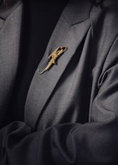 A person is wearing a dark suit jacket adorned with a decorative gold brooch shaped like an umbrella. The brooch is intricately designed and stands out against the dark fabric of the clothing.