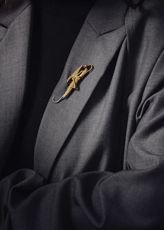Close-up of a golden Ogooué Business Club lapel pin on a black suit jacket.