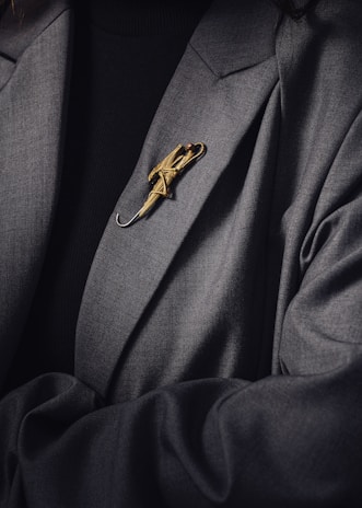 A person is wearing a dark suit jacket adorned with a decorative gold brooch shaped like an umbrella. The brooch is intricately designed and stands out against the dark fabric of the clothing.