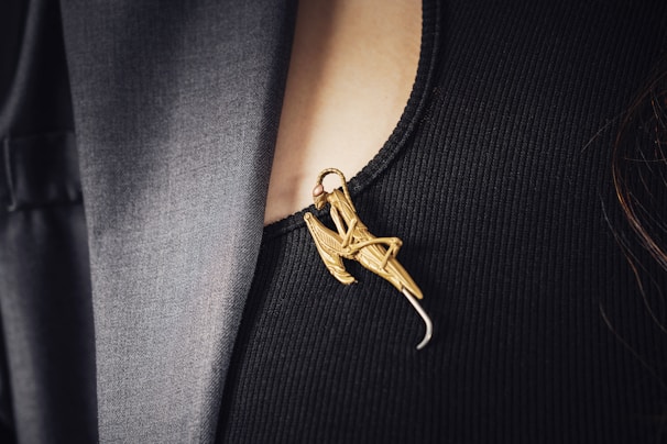 Close-up of a delicate gold brooch on a cream-colored formal dress, highlighting fine craftsmanship.