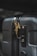 A close-up of a dark-colored suitcase featuring a gold bird-shaped ornament attached to the zipper. The suitcase has a textured surface with visible zippers and a TSA-approved lock. The lighting highlights the ornately designed bird accessory, contrasting against the suitcase's smooth, dark body.