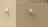 Two surveillance cameras are mounted on a corner of a beige brick building. The cameras are positioned at a right angle to each other and are installed on a cream-colored brick wall. A barren tree branch is visible on the right side.