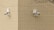 Two surveillance cameras are mounted on a corner of a beige brick building. The cameras are positioned at a right angle to each other and are installed on a cream-colored brick wall. A barren tree branch is visible on the right side.