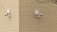 Two surveillance cameras are mounted on a corner of a beige brick building. The cameras are positioned at a right angle to each other and are installed on a cream-colored brick wall. A barren tree branch is visible on the right side.