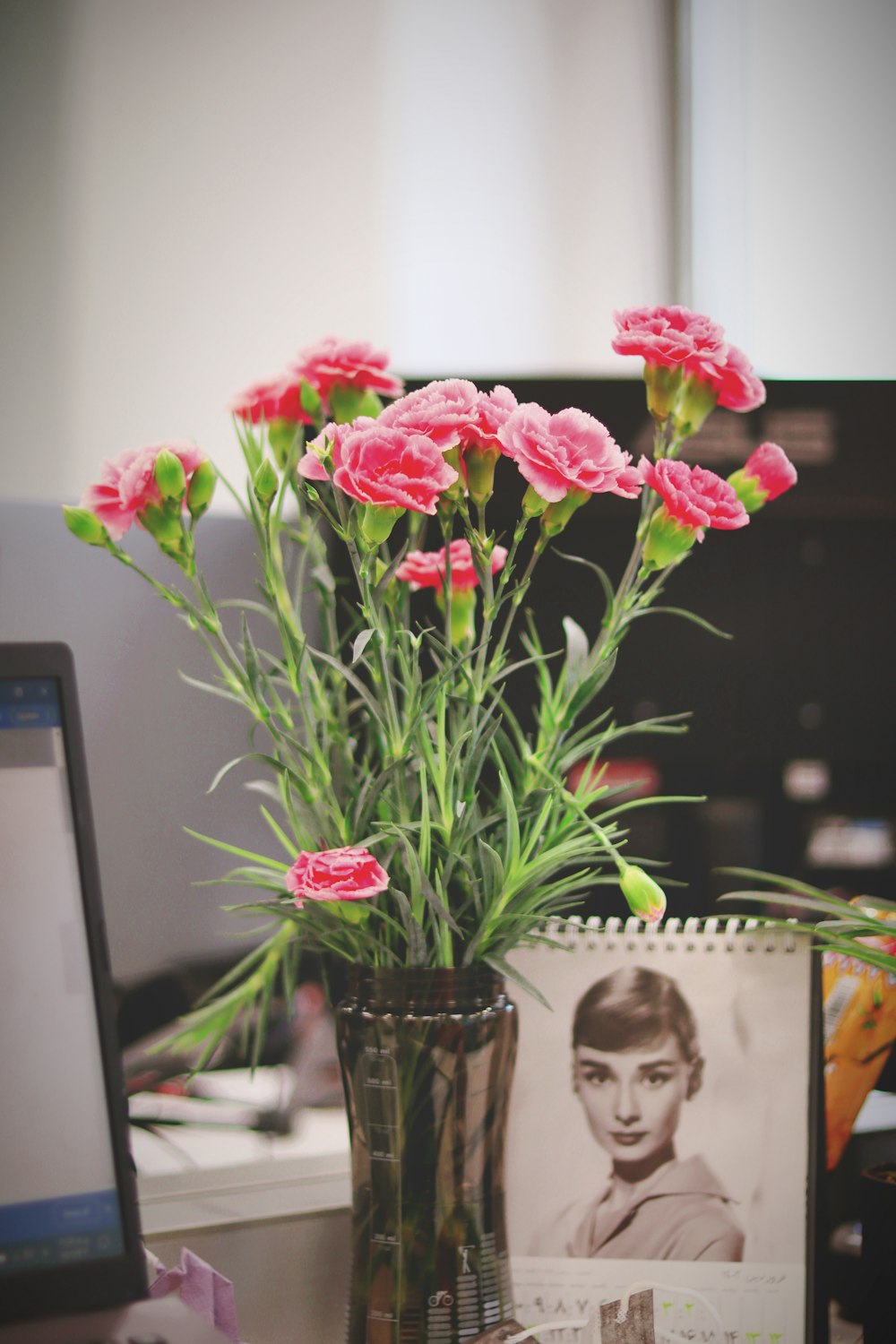 a vase of pink flowers sitting on a desk next to a computer