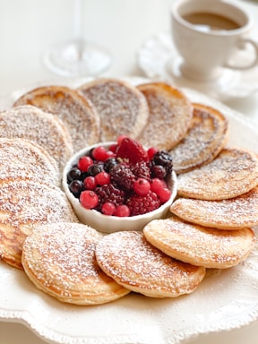 Close-up of a golden Dutch baby pancake topped with fresh berries and a dusting of powdered sugar on a rustic wooden table.