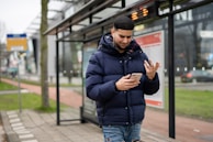 A smiling traveler checking their phone while waiting at a bus station.