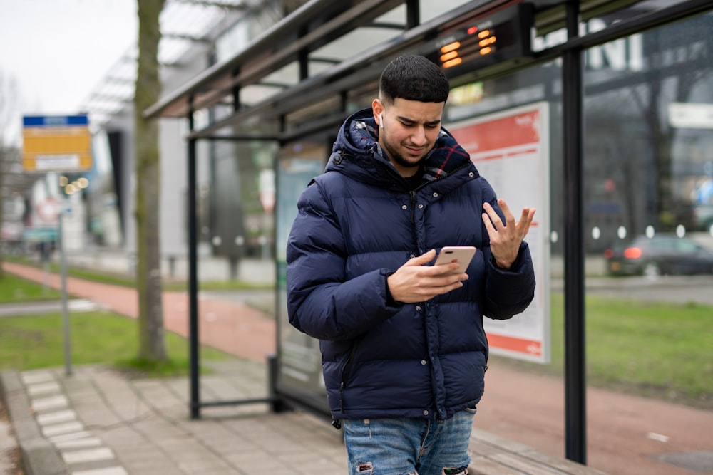 a man standing in front of a bus stop looking at his cell phone