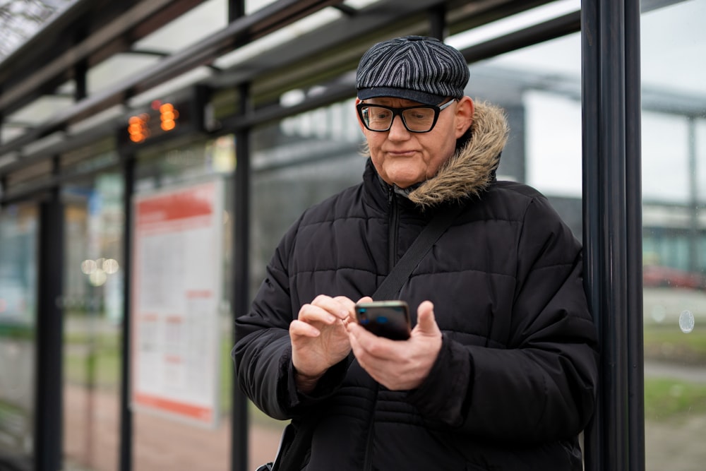 a man in a black jacket and a black hat looking at his cell phone