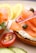 A close-up of a bagel topped with smoked salmon slices, capers, thinly sliced red onions, and a creamy spread. The bagel is accompanied by halves of a cherry tomato, cucumber slices, and lemon wedges. The garnish includes a sprig of fresh dill.